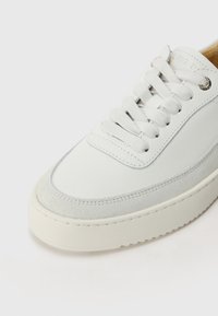 Baskets en cuir blanc avec des accents en daim gris, embout rond et design simple à lacets. Présente une semelle intermédiaire texturée et des détails de couture minimalistes.
