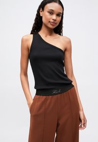 Top negru, cu fante pe umăr, asociat cu pantaloni lejeri, maro, cu talie elastică neagră și detalii brodate.