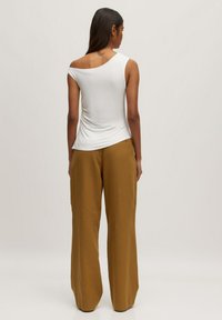 Witte asymmetrische top met een ronde hals, gecombineerd met wijde mosterdkleurige broek. Zachte textuur en ontspannende pasvorm.