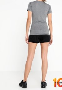 Camiseta gris ajustada de manga corta combinada con pantalones cortos de malla negros. Modelo vistiendo zapatillas deportivas negras, visto desde la espalda.