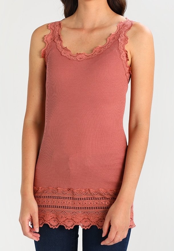 Haut rose saumon sans manches en maille côtelée avec bordure en dentelle au niveau du col, des emmanchures et de l'ourlet, porté avec un pantalon bleu foncé.