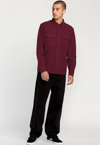 Maroon plaid shirt with long sleeves and two chest pockets, paired with black wide-leg pants and black sneakers. Smooth texture, button closure.