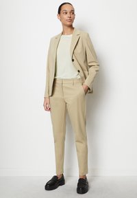 Giacca di suit beige ben tagliata con due grandi bottoni, abbinata a pantaloni fitted coordinati e una camicia di un verde chiaro. Scarpe con plateau nere.