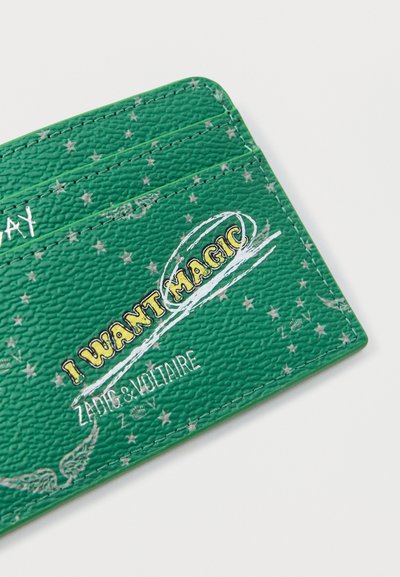 Πράσινος υφασμάτινος θήκη καρτών με ασημένια αστέρια, λευκά σχέδια φτερών και κίτρινο κείμενο "I WANT MAGIC" με το λογότυπο "ZADIG & VOLTAIRE".