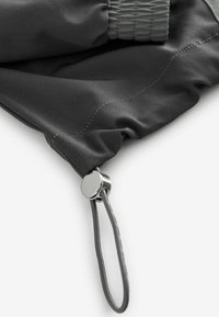 Gray fabric pouch with a gathered top, featuring a silver metallic toggle and cord for closure. Smooth texture with visible stitching detail.
