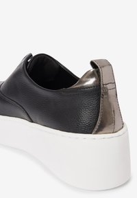 Black leather sneaker with a textured finish, metallic accent at heel, and thick white sole. Design features a smooth, rounded shape.