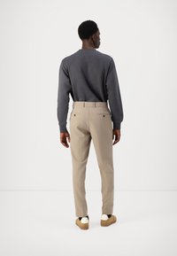 Siva sweatshirt, bež hlače z zadnjimi žepi, gladka tekstura in kontrastni šivi, oblečene s svetlo rjavimi slip-on čevlji, minimalističen dizajn.