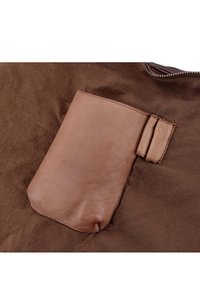 Tessuto marrone con una tasca in pelle. La tasca è di un beige chiaro, rettangolare con bordi arrotondati, cucita alla base in tessuto.