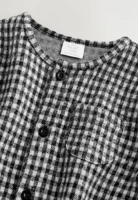 Schwarz-weiße karierte Babykleidung mit rundem Ausschnitt, schwarzen Knöpfen, kleiner Brusttasche und "NEXT baby" Etikett im Kragen.