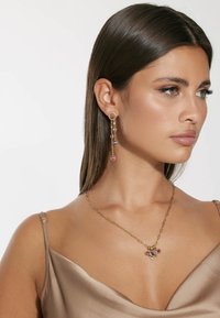 Orecchini color oro con gemme pendenti in rosa e blu. La collana in oro abbinata presenta un grappolo di gemme colorate.