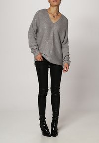 Harmaa neulepusero syvällä V-päällä, pitkät hihat ja rento mitoitus, yhdistettynä mustiin nahkaisisiin skinny-housuihin ja kärkitossuihin.