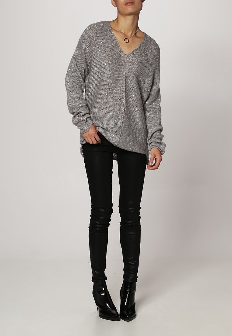 Harmaa neulepusero syvällä V-päällä, pitkät hihat ja rento mitoitus, yhdistettynä mustiin nahkaisisiin skinny-housuihin ja kärkitossuihin.