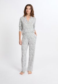 Pyžamo s leopardím vzorem vyrobené z měkkého materiálu. Obsahuje košili s límečkem a knoflíky a kalhoty s elastickým pasem, obojí s šedými skvrnami na bílém pozadí.