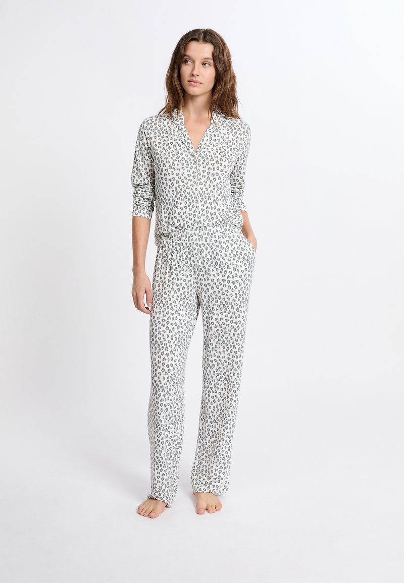 Pyžamo s leopardím vzorem vyrobené z měkkého materiálu. Obsahuje košili s límečkem a knoflíky a kalhoty s elastickým pasem, obojí s šedými skvrnami na bílém pozadí.