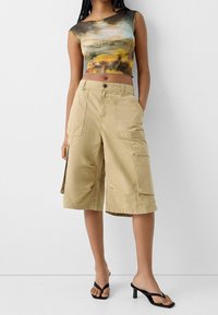 Tvådelad outfit bestående av en figurnära, flerfärgad crop top med ett abstrakt mönster och beigefärgade cargo-shorts knälång med flera fickor.