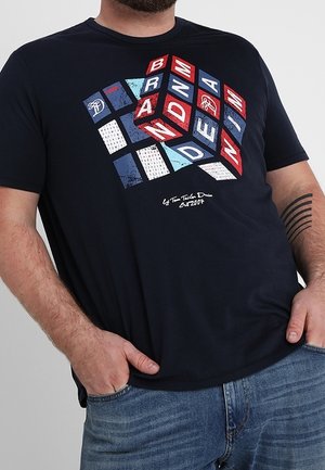 Mørkeblå t-shirt lavet af bomuld med et grafisk design bestående af røde, hvide og blå blokke, der danner ordene "BRAND" og "DENIM." Kortærmet.