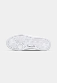 Baldalkio batų iš baltos gumos pado, su zigzago raštu ir apvalioniškai akcentais. Logo "LACOSTE" atspausdintas šalia kulno.