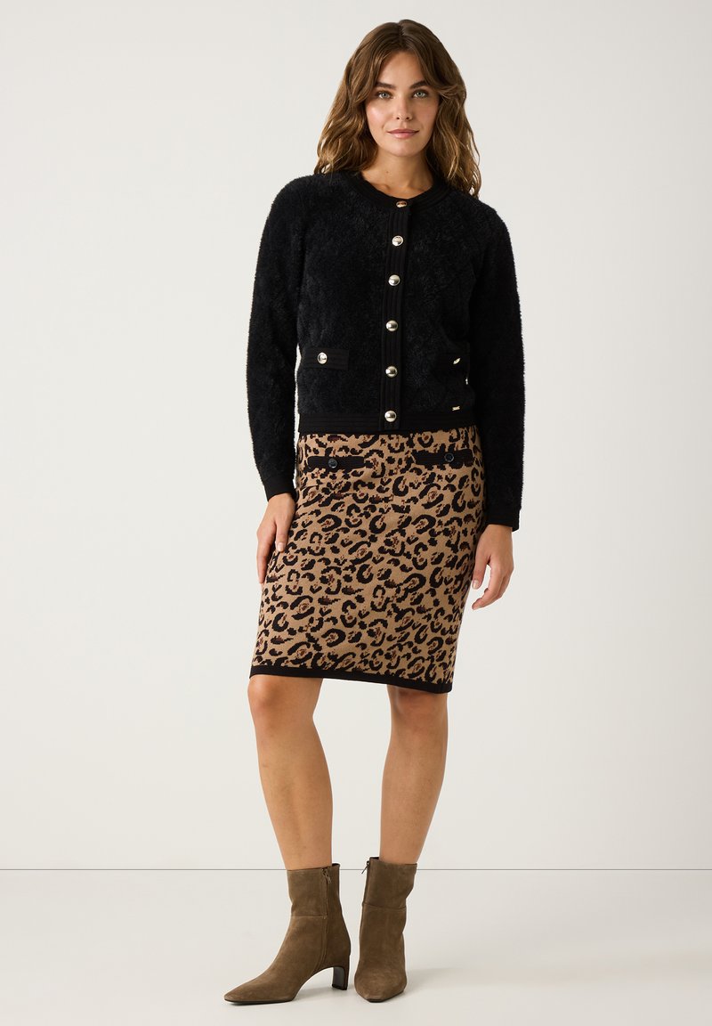 Schwarze flauschige Strickjacke mit goldenen Knöpfen, kombiniert mit einem Bleistiftrock im Leopardenmuster in Beige und Schwarz und olivgrünen Ankle Boots mit Blockabsatz.