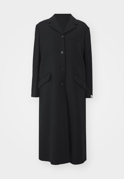 Casaco longo preto feito de lã, com colarinho em bico, cinco botões, dois bolsos laterais e um bolso no peito.