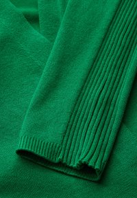 Maglione verde lavorato a maglia con texture liscia e polsini a coste, design a V e costruzione senza cuciture.