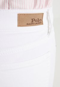 Jeans bianchi con una consistenza liscia, dotati di un'etichetta in pelle marrone con la scritta "Polo Ralph Lauren" in rilievo sulla cinta posteriore.