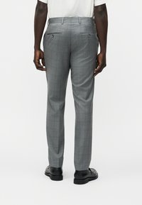 Homme portant un pantalon habillé gris et des chaussures habillées noires, debout de dos, les mains détendues le long du corps.