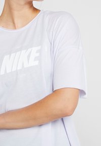 Camiseta de Nike en púrpura claro con mangas cortas, que presenta un gran logo blanco impreso en la parte delantera. Tejido suave y ligero, con corte holgado.