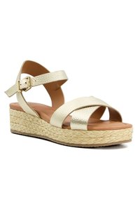 Sandale à plateforme en cuir texturé doré avec une semelle en paille tissée. Elle présente des brides entrecroisées et une fermeture à boucle à la cheville.