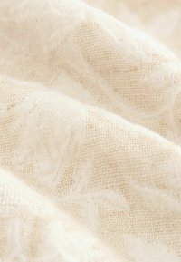 Tela de color beige claro con un tejido texturizado, que presenta sutiles patrones de hojas. Material suave y ligeramente translúcido, creando una apariencia delicada.