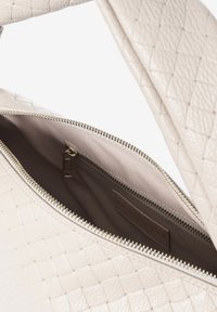 Sac à main en cuir tissé blanc avec une fermeture éclair sur le dessus, présentant une doublure en tissu lisse et une poche intérieure avec fermeture éclair.