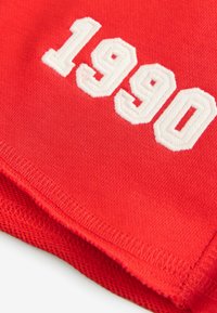 Rød stof med det broderede nummer "1990" i hvid, med en struktureret finish og rene kanter.