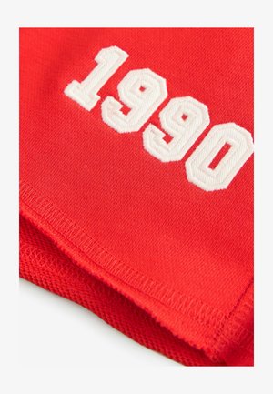 Raudona medžiaga su baltu siuvinėtu numeriu "1990", su tekstūruotu paviršiumi ir tvarkingais kraštais.