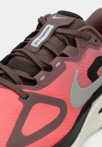 Αθλητικό παπούτσι Nike με ροζ και καφέ διχτυωτή επιφάνεια, γκρι λεπτομέρειες, αναπνεύσιμη υφή και μαλακό πέλμα με διακοσμητικό μοτίβο.