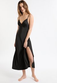 Vestido negro de satén con un escote en V profundo, tirantes finos y una apertura lateral alta hasta el muslo. Textura suave y diseño fluido.