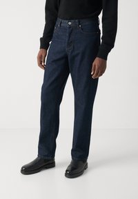 Mørkeblå denimjeans med rett ben-design, iført en svart genser og svarte skinnsko, med standard lommer og søm.