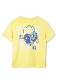 T-shirt jaune vif avec un personnage de donut cartoon amusant portant des écouteurs, accompagné du texte "MEILLEURE HUMEUR" et de phrases fantaisistes en arrière-plan.