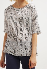 Blusa a maniche corte in tessuto leggero, con un motivo geometrico blu navy, beige e crema. Collo rotondo con vestibilità comoda.