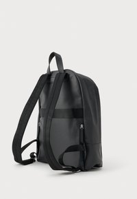 Juodas dirbtinio odos kuprinės modelis su reguliuojamais diržais, apvalia forma, dviem užtrauktukais uždaromomis šoniniais kišenėmis ir tekstūruotu paviršiumi.