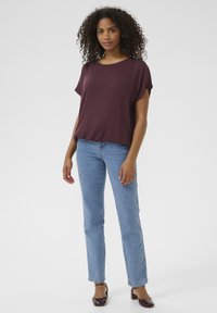Bordeaux farbenes Kurzarmoberteil mit lockerer Passform, kombiniert mit hellblauen, geraden Jeans und dunklen Schuhen. Glatte Textur, lässiges Design.