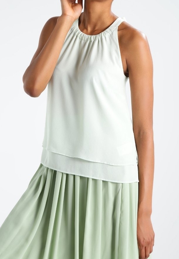 Světle zelená bezramínková blůza s nabíraným výstřihem, vrstveným designem a průhlednou tkaninou; v kombinaci s odpovídající plisovanou sukní.