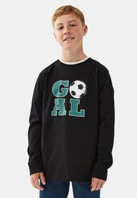 Schwarzes Langarm-T-Shirt mit der Aufschrift "GOAL" in grünen Buchstaben und einer weißen Fußballgrafik, runder Ausschnitt und lässige Passform.