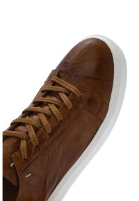 Bruine leren sneaker met bijpassende bruine veters en dikke witte rubberen zool, bovenaanzicht en zijaanzicht tegen een witte achtergrond.