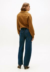 Bruine pullover met hoge kraag en afgezakte schouders, gecombineerd met blauwe wijde jeans met achterzakken en een tan leren label.