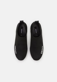 Svarta slip-on skor med en elastisk stickad ovandel, med en framträdande vit "DKNY"-logotyp på sidan och bakre dragöglor för enkel påtagning.