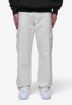 Beige cargobroek met meerdere zakken, rechtlijnig ontwerp, gestikte details en een ontspannen pasvorm, gecombineerd met witte sneakers.