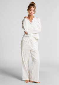 Witte pyjamaset met een lange mouw, knoopsluiting en een zak, en losse broek, beide versierd met kleine blauwe stippen.