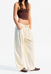 Brown cropped bodysuit, white wide-leg pants with drawstring, and brown shoes with silver accents, against a white background.