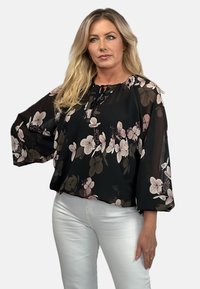 Czarna bluzka w kwiaty z dużymi, zwiewnymi rękawami. Posiada okrągły dekolt z zapięciem na wiązanie, ozdobiona różowymi i kremowymi wzorami kwiatowymi.