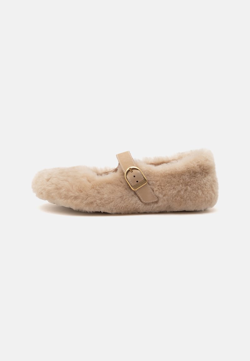 Chaussure plate beige duveteuse avec une texture douce en fourrure, dotée d'une bride beige unique avec une boucle dorée sur le dessus.