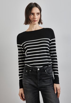 Pull rayé noir et blanc avec un décolleté bateau large, fabriqué à partir d'un matériau doux. Associé à un jean gris foncé taille haute.